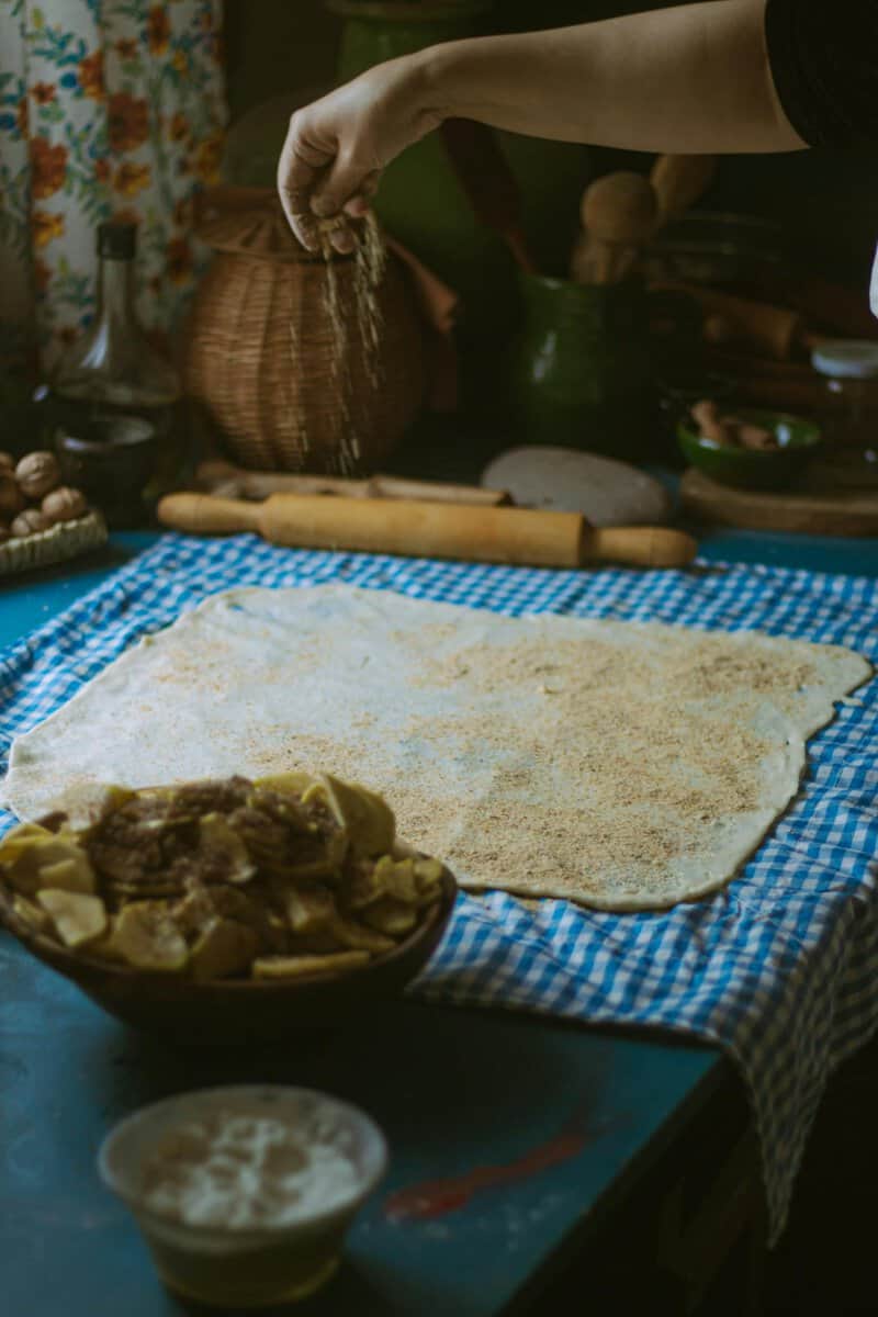 Hand sprinkling ingredients onto dough in a cozy kitchen setting, creating a rustic feel.