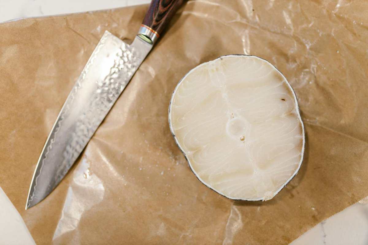 Overhead shot of a fresh piece of fish with a knife on brown butcher paper.